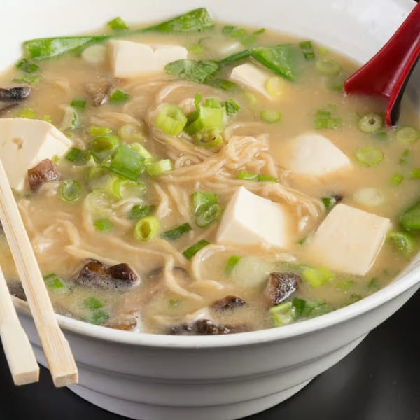 Close-up of a bowl of Vietnamese noodle soup with tofu, mushrooms, and green onions.