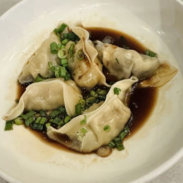 Steamed dumplings in a savory sauce, garnished with fresh green onions, served in a white bowl.