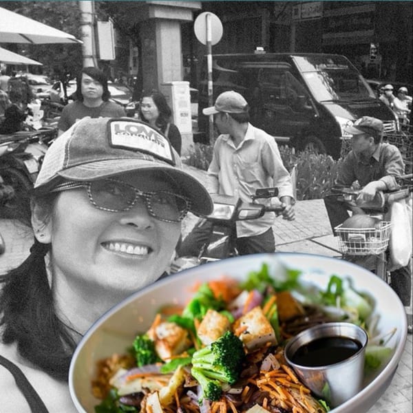 Smiling woman in sunglasses and cap with a colorful Vietnamese noodle bowl in the foreground.