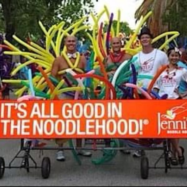 Jenni's Noodle House parade float with people in colorful balloon costumes and a large banner.