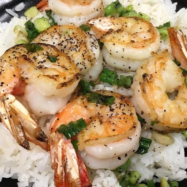 Close-up of grilled shrimp with black pepper and green onions over white rice.